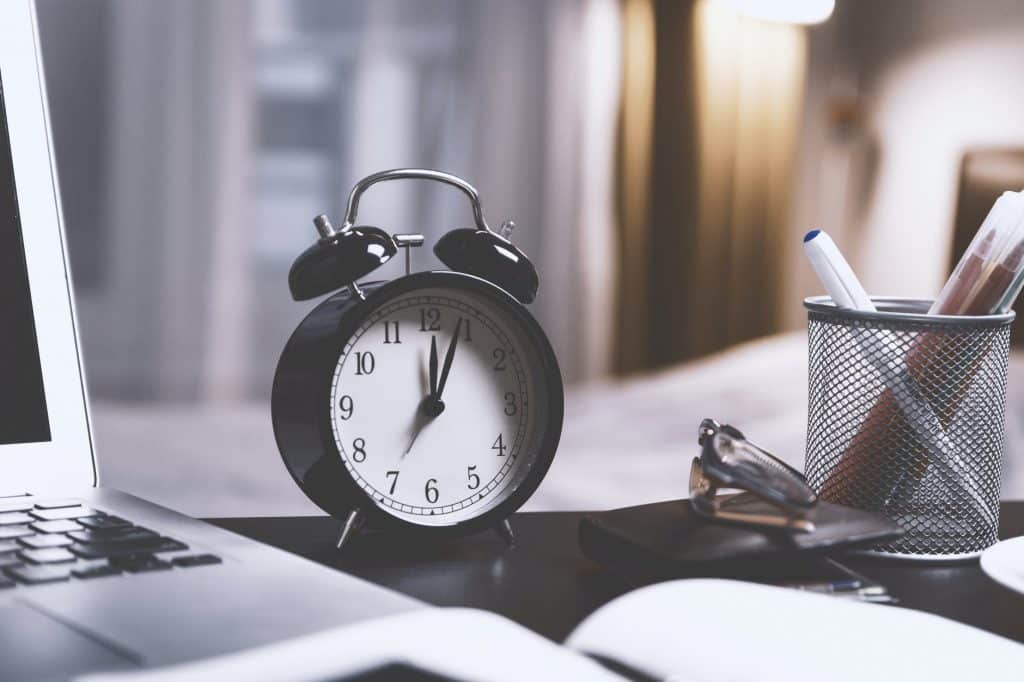 A clock on a desk beside a computer.