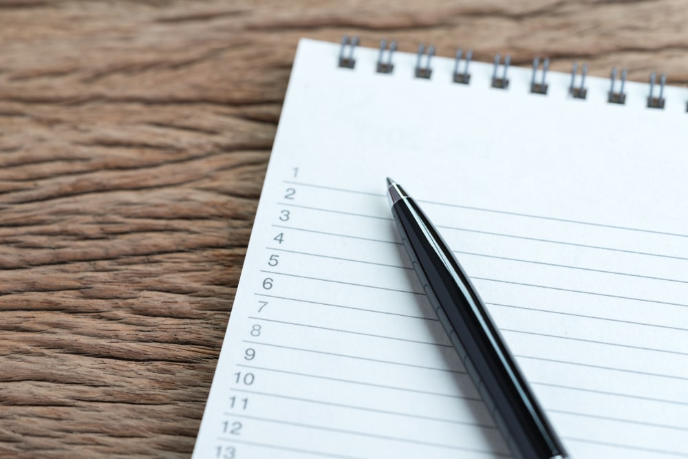 A pen laying on top of a pad of paper open to a page with a blank list.