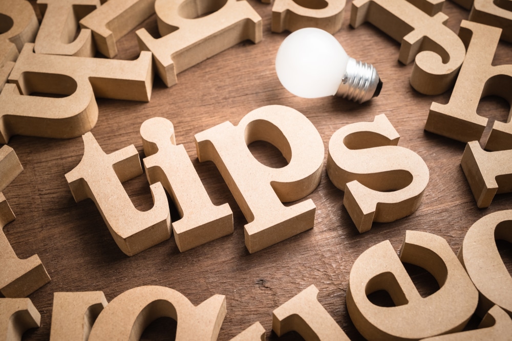 Wooden letters laying on a table, spelling out "tips," and lit by a lightbulb.