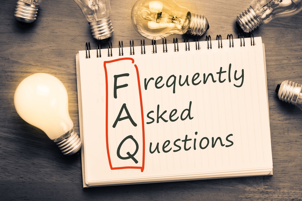 "Frequently Asked Questions" written on a notepad on a table with surrounding lightbulbs.