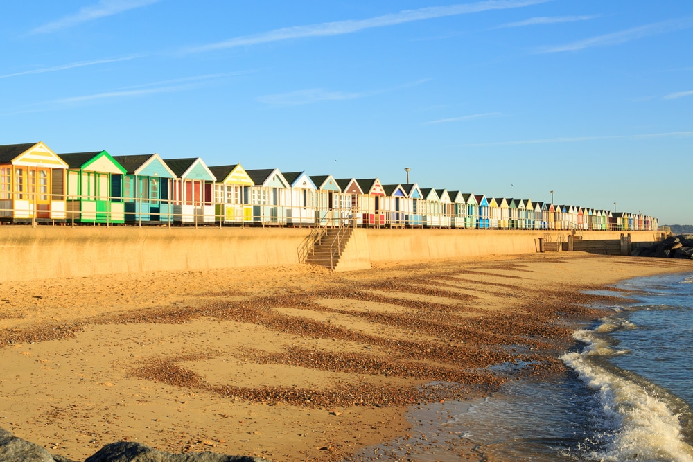 Empty beach in Suffolk with a row of colorful houses behind it.