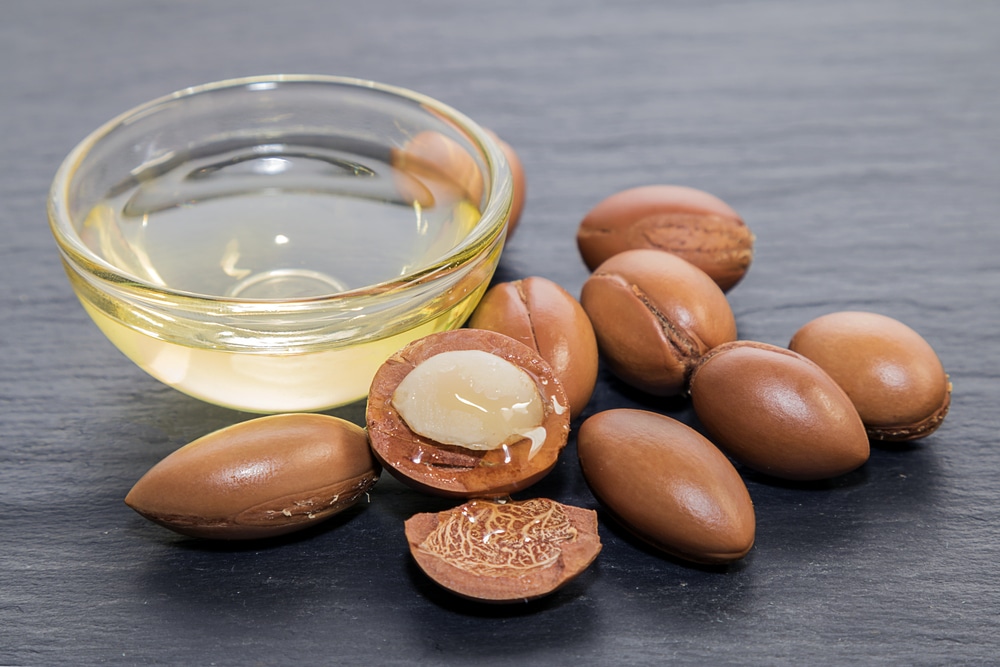 Argan oil in a bowl, and the argan tree fruit on a table.