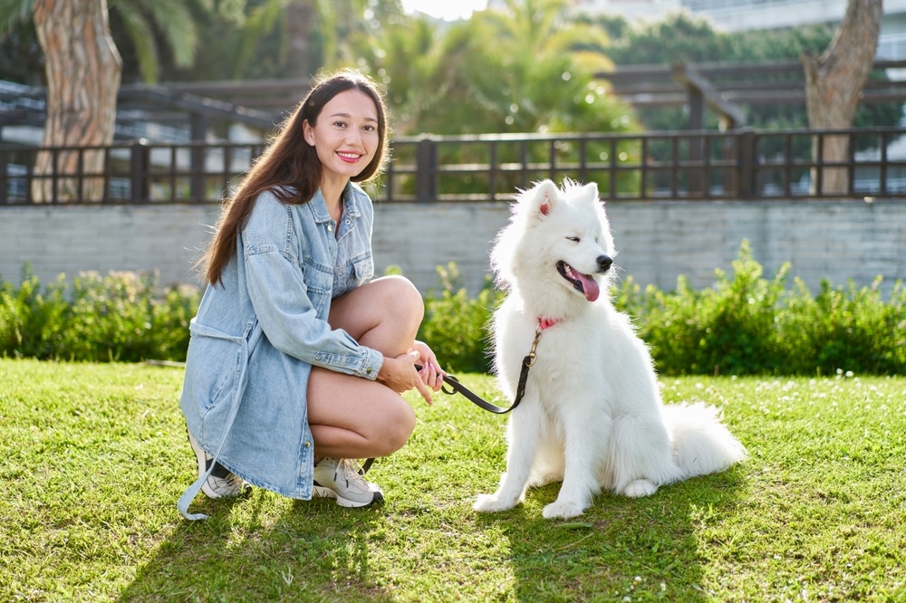 A woman with her dog on a leash outside.