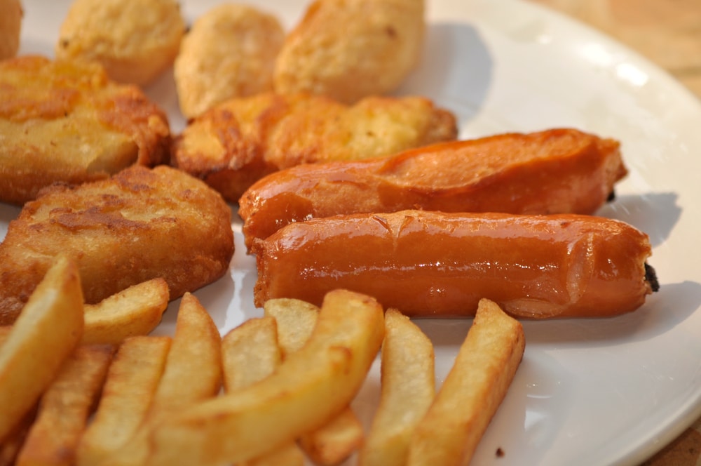 Processed food on a plate, including chicken nuggets, hot dogs, and fries.