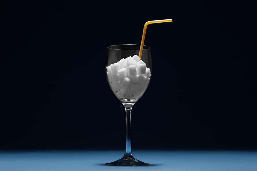 A wine glass with sugar alcohol cubes and a straw in it.