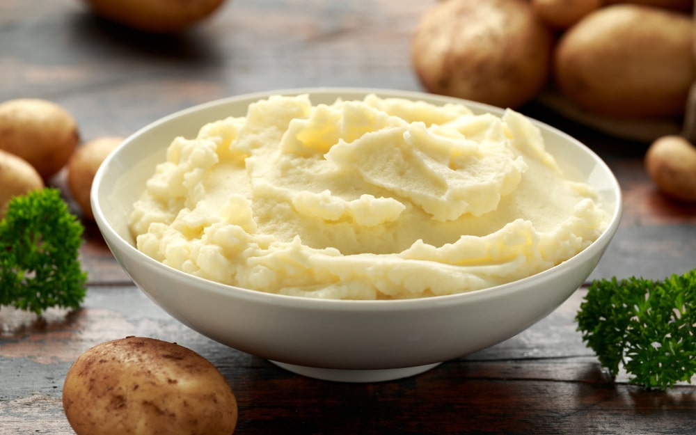 A bowl of mashed potatoes with some potatoes around it.
