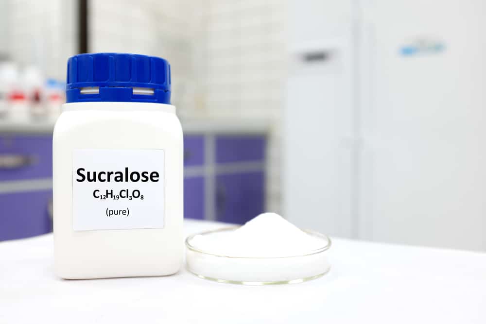A bottle of sucralose with some of it in a petri dish next to it.