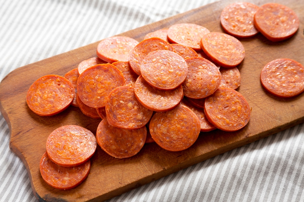 A pile of pepperoni spread out over a cutting board.