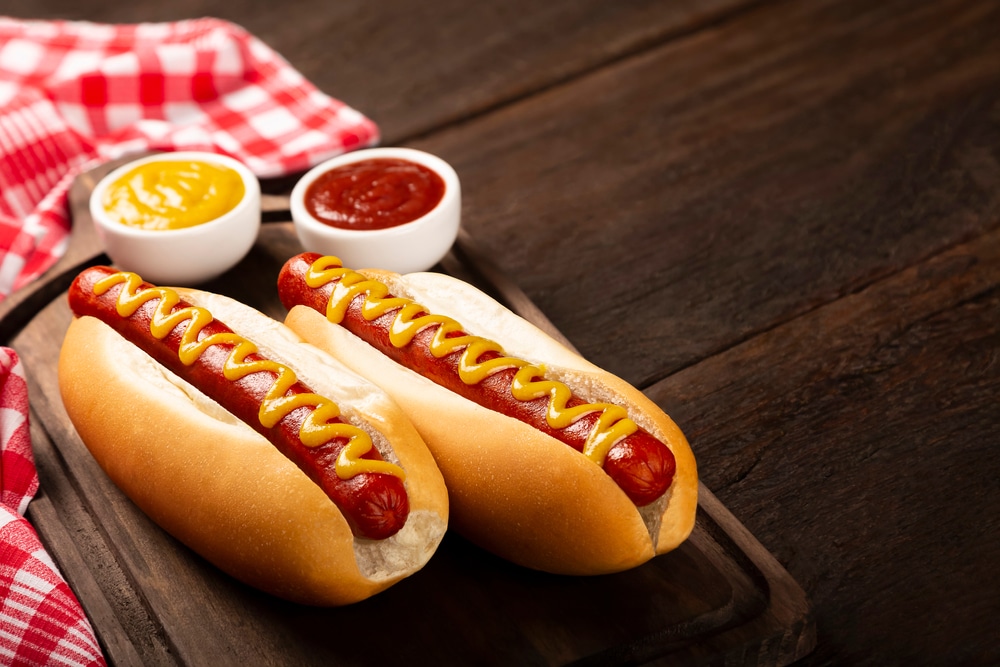 Two hot dogs sitting on a plate with some ketchup and mustard next to them.