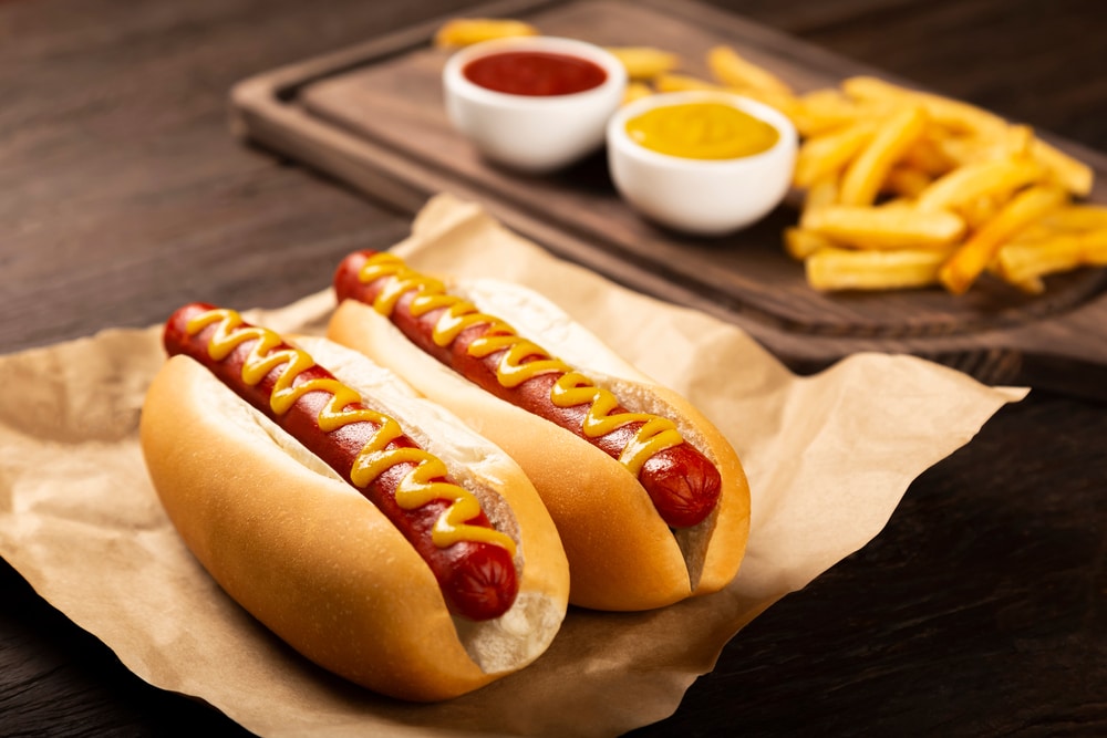 Two hot dogs laid out on a table with some fries and condiments nearby.
