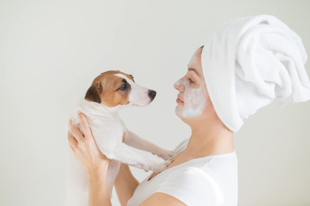 An owner doing a facial home spa treatment while holding and looking at their dog.