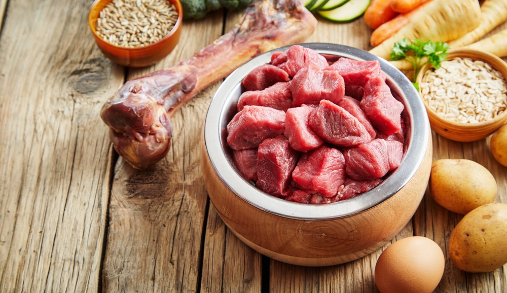 A bowl of meat with other foods sitting nearby.