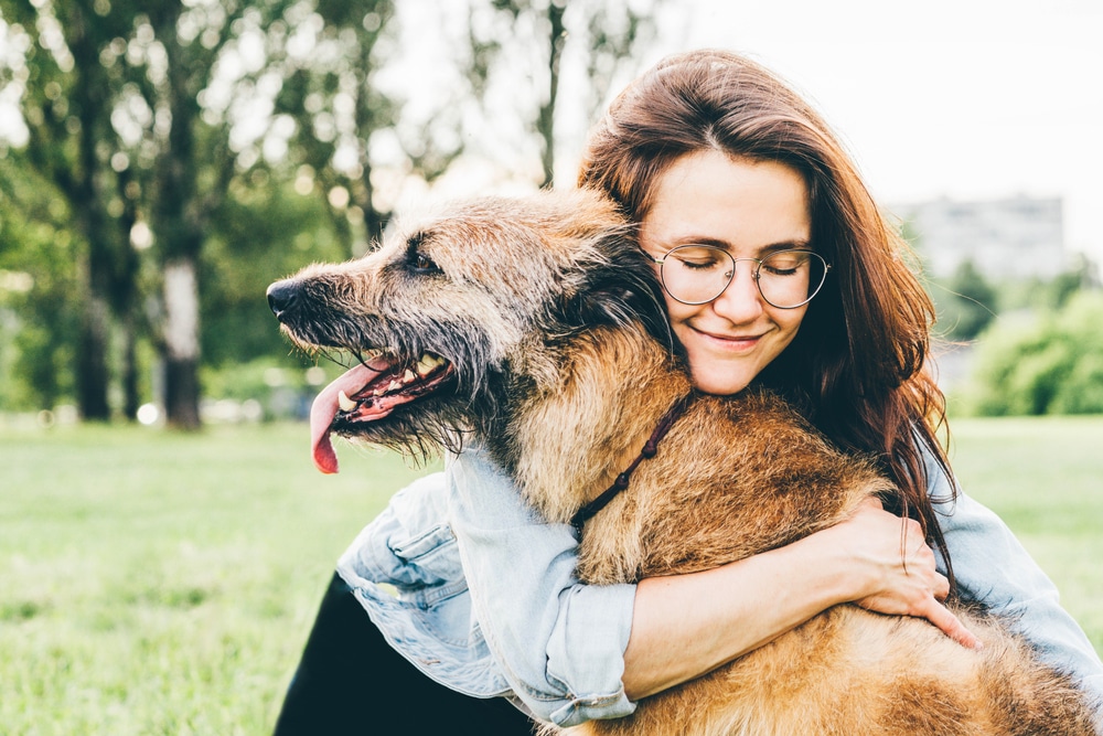 An owner hugging her older dog outside.